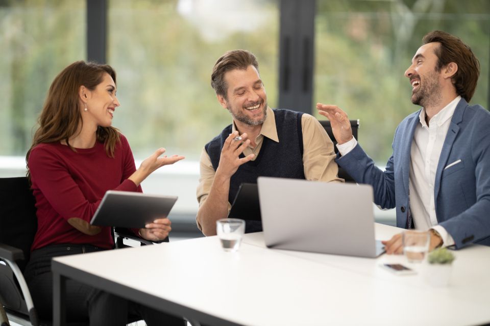 A smiling team discussing ideas around a laptop in a bright, modern office