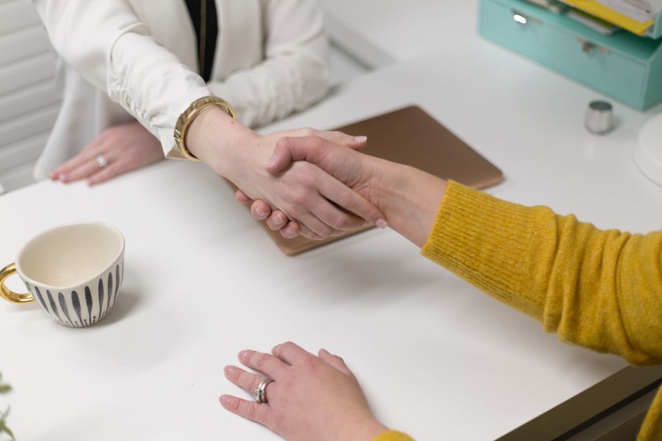 Two people shaking hands across a desk at the start of a working partnership